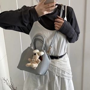 Detail of light blue lychee leather handbag with cute plush dog pendant on a model