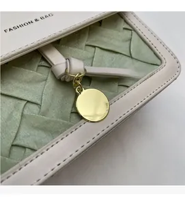 Close-up of woven texture on green and cream shoulder bag with golden metal charm detail