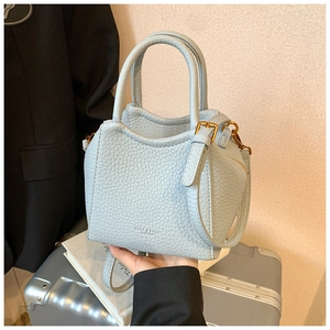 Detail of light blue textured leather handbag with logo lettering and metal zipper
