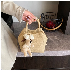 Detail of cream crossbody bag with litchi texture and a cute white dog plush charm