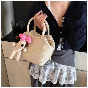 Detail of off-white lychee leather handbag with a cute dog plush charm and golden D-ring