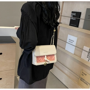 Detail of a woven crossbody bag with cream and pink textures and a gold chain strap