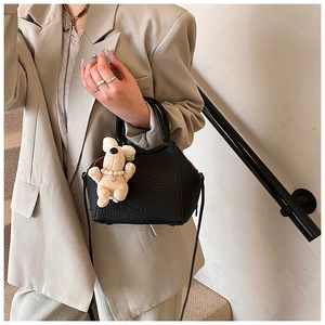 Close-up of black lychee leather crossbody bag featuring a cute beige puppy plush charm