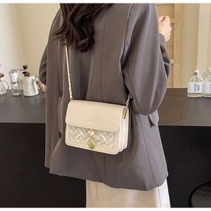 Detail of a beige quilted crossbody bag with a gold chain strap shown on a model