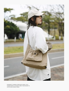 Street style shot of a khaki canvas messenger bag with functional side drawstrings
