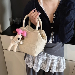 Close-up of beige lychee textured bucket bag with cute puppy plush charm and gold hardware
