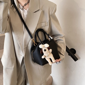 Close-up of black lychee leather bucket bag with cute puppy charm and gold zipper detail