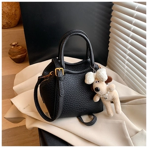 Minimalist black lychee leather bucket tote bag with cute plush puppy charm on beige coat