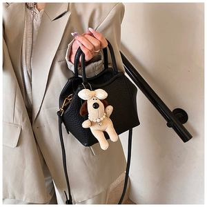Detail of black pebbled leather handbag with cute plush puppy charm on a metal zipper