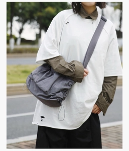 Detail of grey nylon drawstring crossbody bag paired with layered casual street style outfit