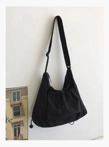 Detail of minimalist black canvas tote bag showing drawstring pocket and wide nylon strap