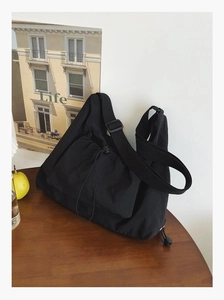 Detail of black nylon tote bag featuring drawstring outer pocket and adjustable shoulder strap