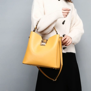 Detail of bright yellow bucket bag with snakeskin texture handle and gold clasp closure