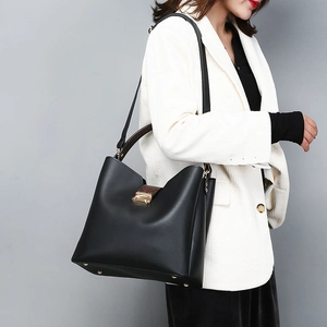Detail of black faux leather handbag with metal buckle and adjustable strap on a model