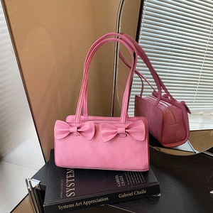 Pink rectangular shoulder bag with decorative bows and double straps on an art book