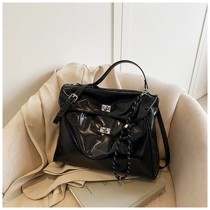 Detail of black patent leather tote bag featuring dual silver twist locks and woven cord