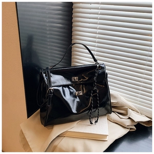 Detail of glossy black leather tote bag featuring a metallic lock and braided rope decor