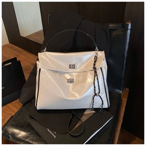 Detail of a creamy white glossy patent leather tote with silver buckles on a black chair