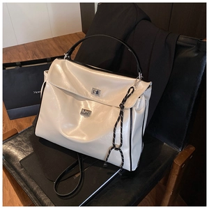 Detail view of cream shoulder bag featuring silver twist locks and braided charm