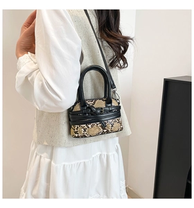 Detailed view of mini snake pattern handbag with black leather handle on female model
