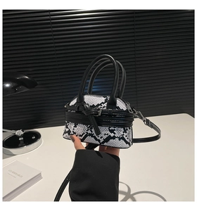 Close-up of mini snakeskin texture shell bag with black handle and strap in a minimalist setting