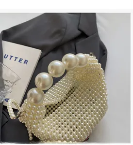 Detail of handcrafted cream pearl handbag with woven handle on a grey blazer background