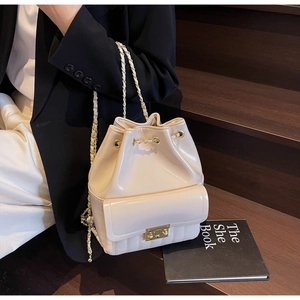 Close-up of cream bucket bag with gold chain strap and drawstring closure on wooden stairs