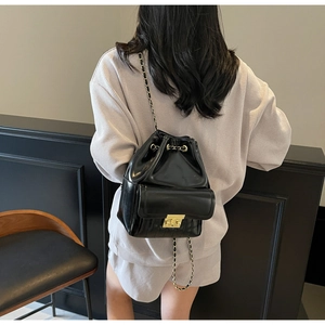 Detail of black glossy drawstring backpack with gold chain straps on a model back