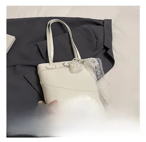 Detail of cream leather bucket bag featuring lace bow and pearl charm accessories