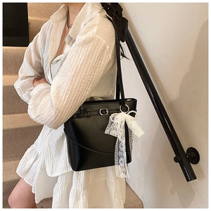 Detail of black bucket bag with white lace bow and pearl pendant on a shoulder strap