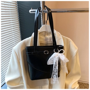 Detail of black faux leather tote bag with elegant white lace bow and pearl charm