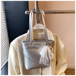 Detail of silver bucket bag with white lace bow, pearl pendant and metal buckle on suit