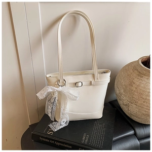 Detail of cream white bucket bag with leather buckle and lace bow on textured books