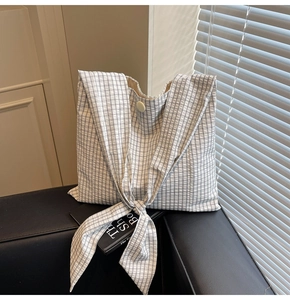 Detail of checkered tote bag featuring a bow shoulder strap and single button closure