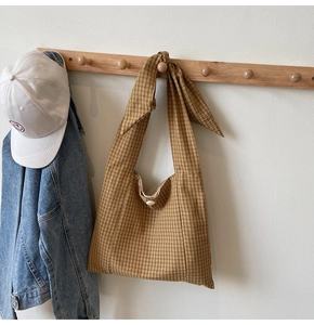 Detail of checkered fabric tote bag with knotted shoulder strap and button closure