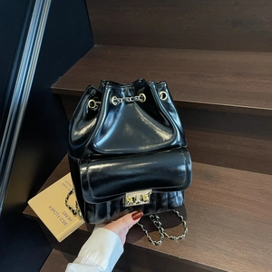 Glossy black leather bucket backpack with chain drawstring and metal lock on wooden stairs