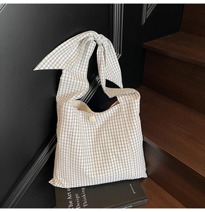 Detail of black and white plaid tote bag featuring a decorative bow-tie shoulder strap