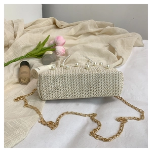 Detail of cream straw woven bag featuring large faux pearl trim and golden chain strap