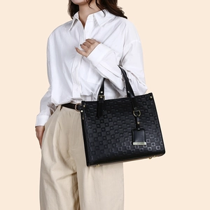 Close-up of black quilted tote bag with gold hardware and logo tag on a female model