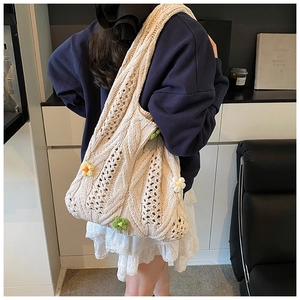 Detail of hollow woven tote bag with 3D floral accents on a beige knit texture