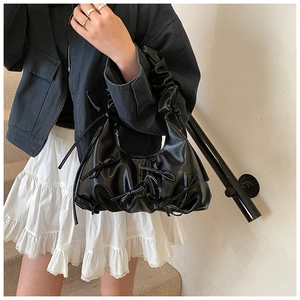 Detail of black pleated hobo bag with bow accents and glossy PU leather texture