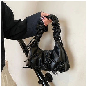 Close-up of black pleated cloud bag with ribbon bow accents and metallic zipper detail