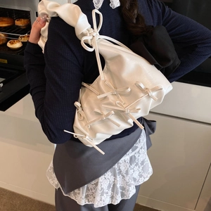 White pleated cloud shoulder bag with bow accents worn by a model in a cozy kitchen