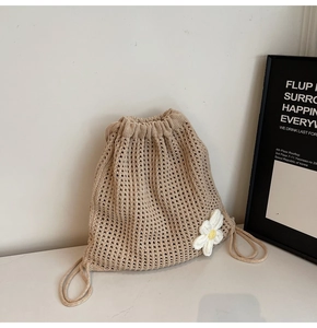Detail of beige knit drawstring bag featuring handmade white flowers and hollow texture