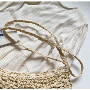 Detailed close-up of a beige hollow-out woven straw bag with thin shoulder straps