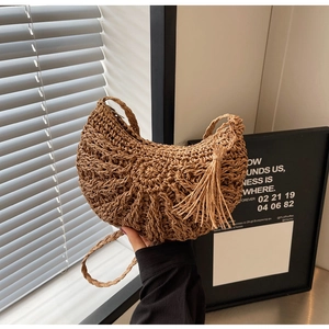 Close-up of brown woven straw shoulder bag featuring fringe detail and hollow pattern