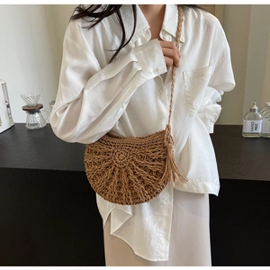 Detail of hand-woven straw crossbody bag with tassels and shoulder strap on a model