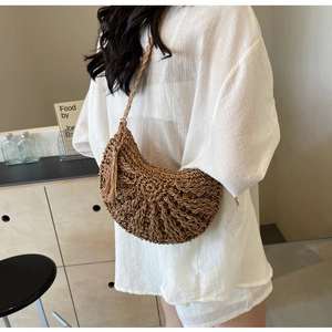 Detail of hollow woven straw bag with crescent shape and stylish tassel pendant