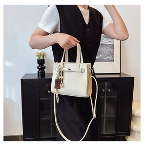 Detail of cream white pebbled leather handbag with metallic lock and silk scarf accent