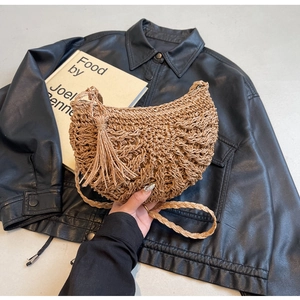 Close-up of crescent woven straw bag featuring intricate cutout patterns and long tassels